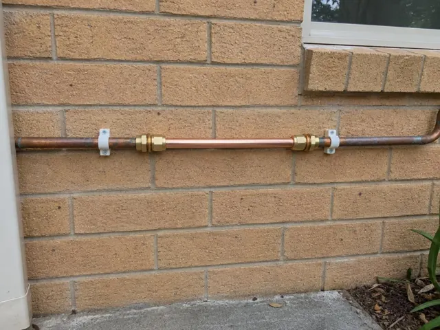 Repaired copper water pipe on an exterior brick wall with brackets and a window above in Manly Vale